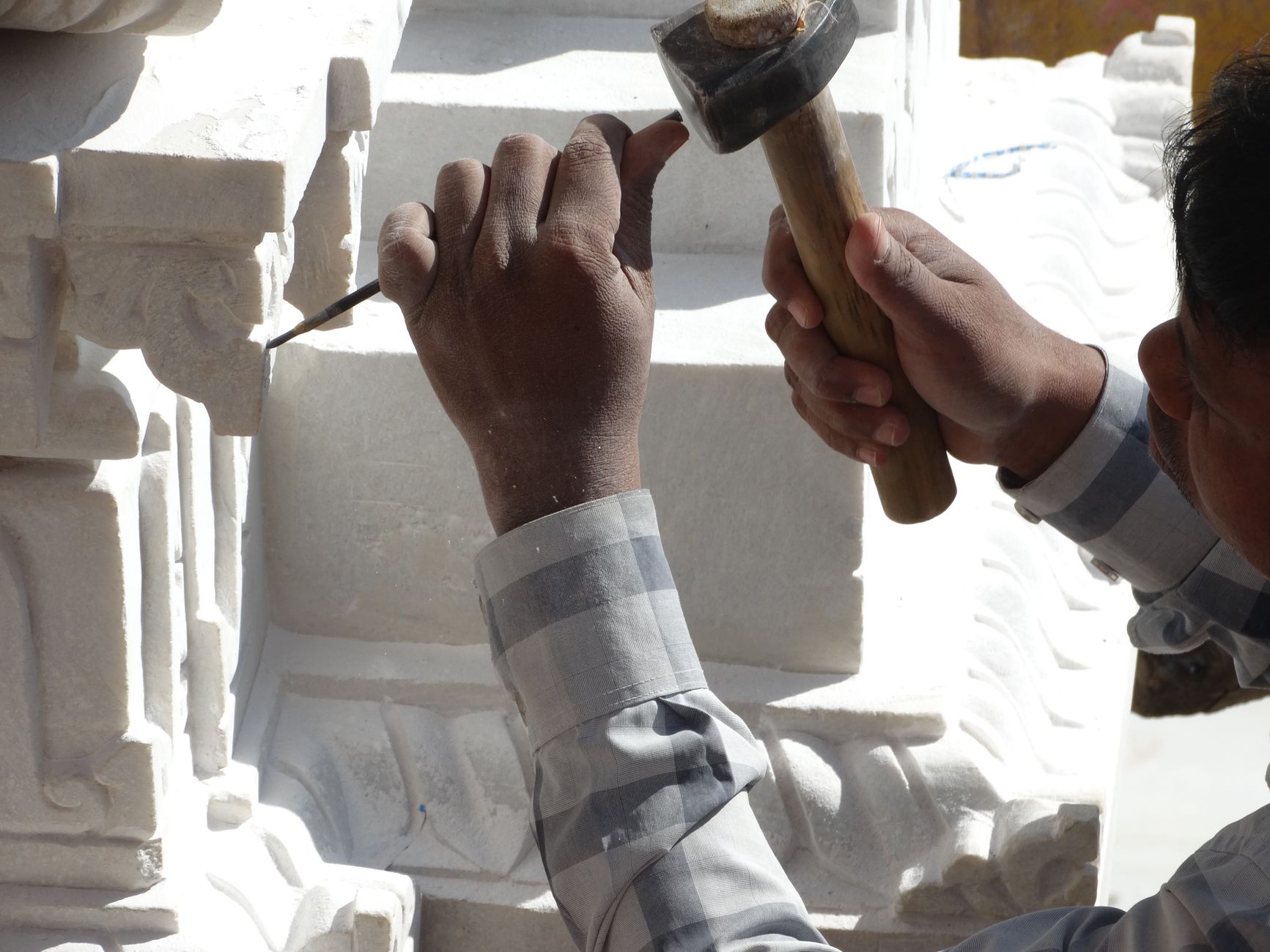 Two hands working a pale stone block with a hammer and chisel